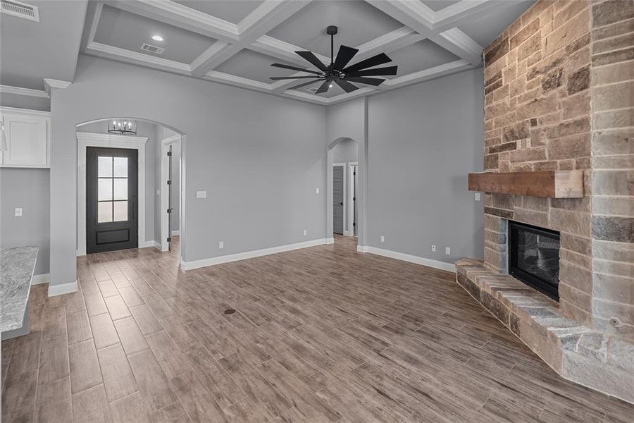 Unfurnished living room with hardwood / wood-style flooring, a stone fireplace, beam ceiling, ceiling fan, and coffered ceiling