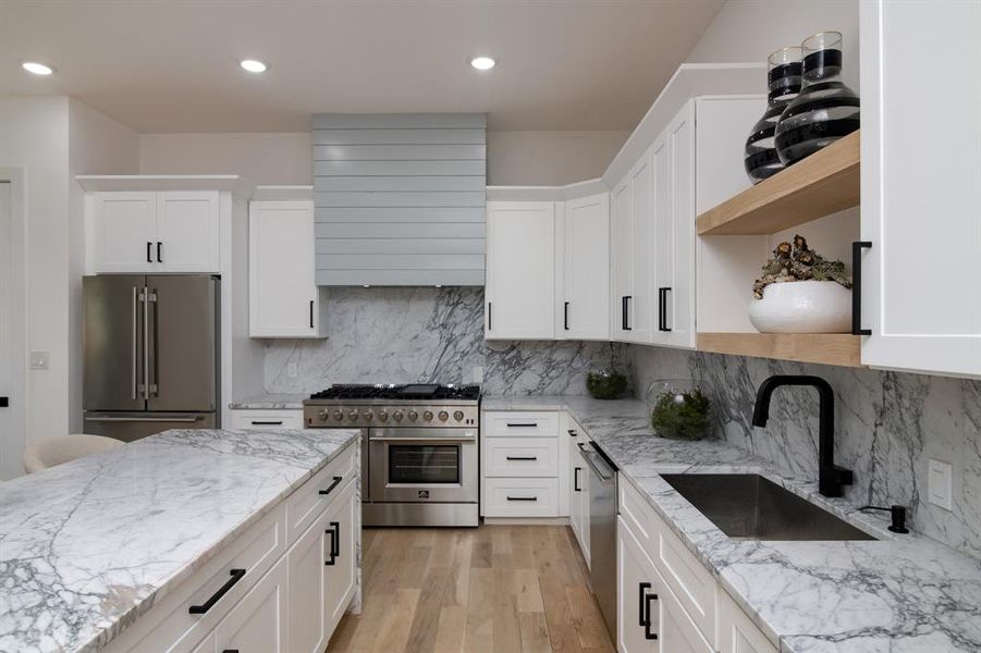 Kitchen with high end appliances, white cabinets, sink, light stone countertops, and light hardwood / wood-style flooring