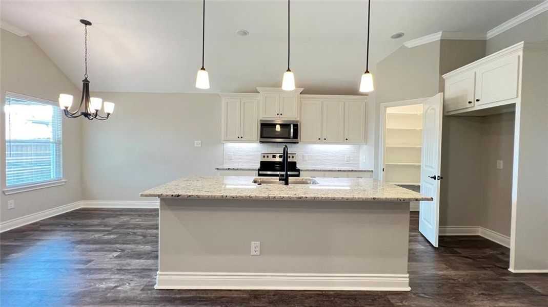 Kitchen featuring light stone countertops, white cabinetry, appliances with stainless steel finishes, and decorative light fixtures