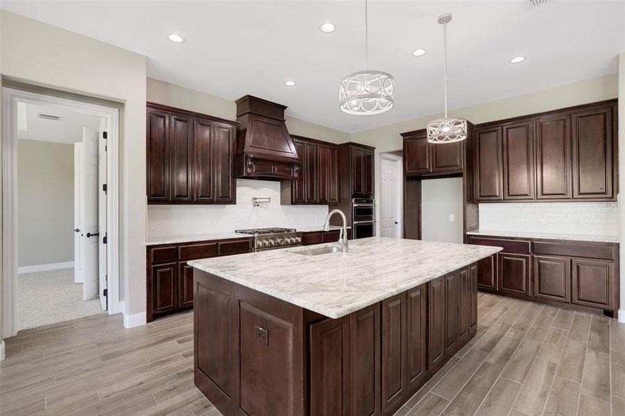 Kitchen featuring custom range hood, a kitchen island with sink, hanging light fixtures, light carpet, and sink