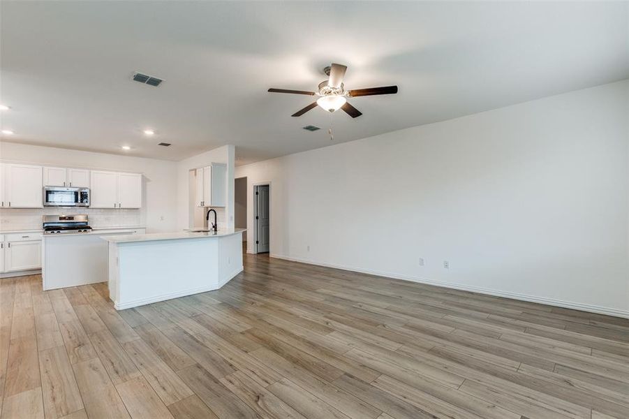 Kitchen featuring stainless steel appliances, light hardwood / wood-style floors, a kitchen island with sink, backsplash, and white cabinetry