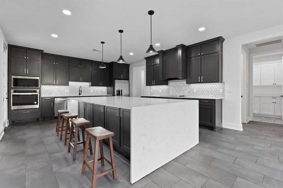 Kitchen featuring light tile patterned flooring, stainless steel appliances, hanging light fixtures, decorative backsplash, and a spacious island