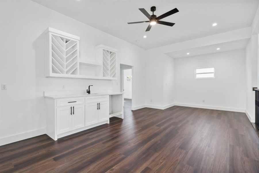 Unfurnished living room with dark wood-type flooring, indoor wet bar, and ceiling fan