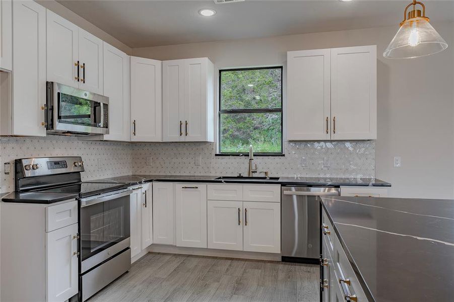 Kitchen with tasteful backsplash, stainless steel appliances, light wood-type flooring, pendant lighting, and sink