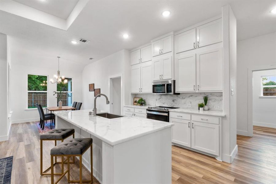 Kitchen featuring a kitchen island with sink, light wood-type flooring, sink, appliances with stainless steel finishes, and white cabinetry