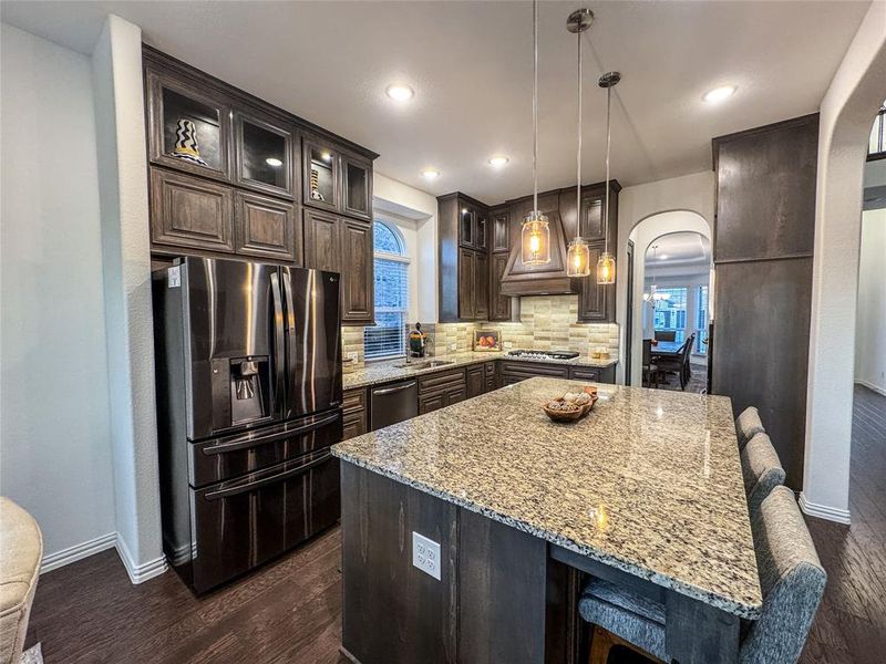 Kitchen featuring appliances with stainless steel finishes, a kitchen island, backsplash, pendant lighting, and dark wood-type flooring