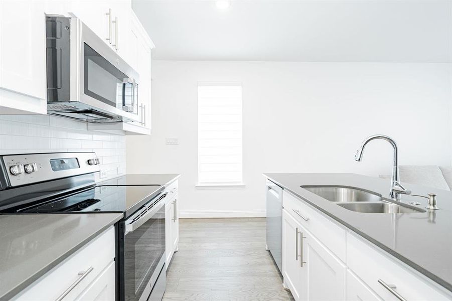 Kitchen with light hardwood / wood-style floors, stainless steel appliances, tasteful backsplash, white cabinets, and sink
