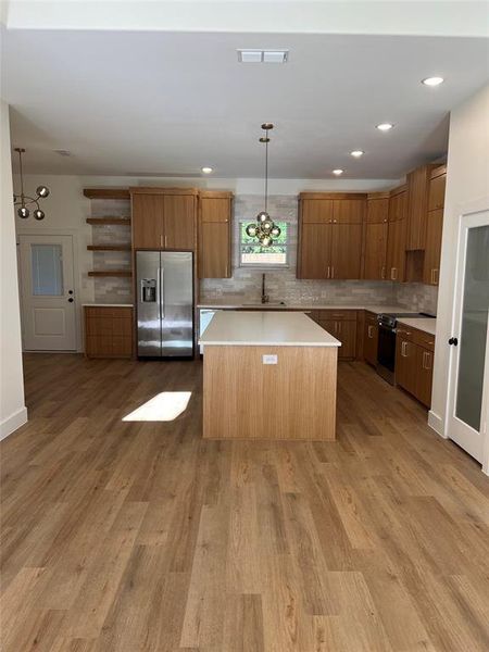 Kitchen featuring stainless steel appliances, pendant lighting, a center island, light wood-type flooring, and decorative backsplash