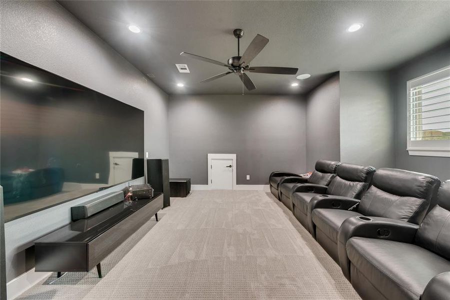 Carpeted cinema room with ceiling fan