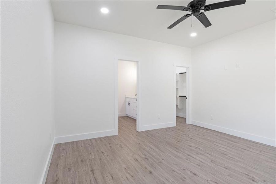 Unfurnished bedroom featuring light wood-type flooring, ensuite bath, a spacious closet, a closet, and ceiling fan
