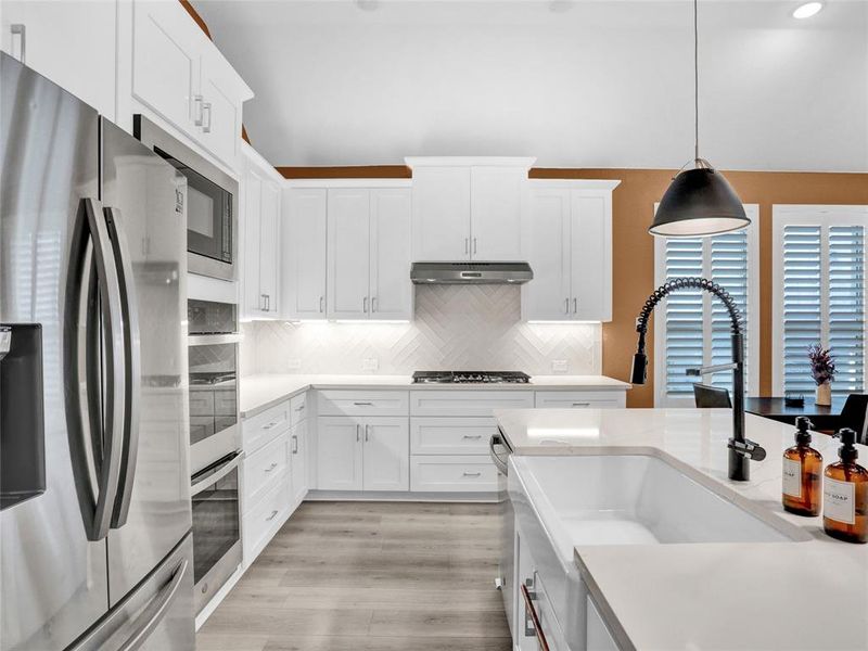 Gorgeous modern kitchen with double ovens, quartz counters, farmhouse sink, island and gas stovetop.