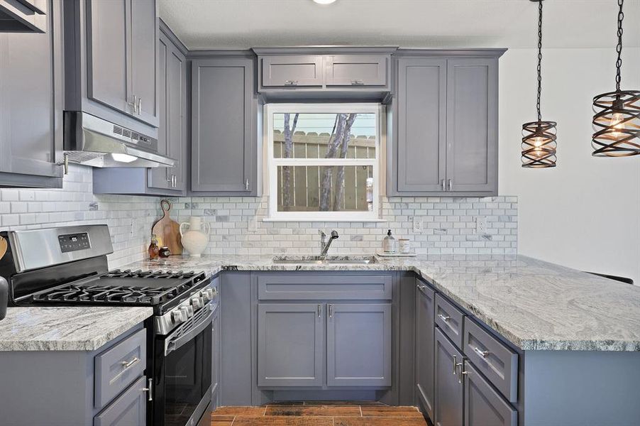 Kitchen featuring stainless steel range with gas cooktop, gray cabinetry, and pendant lighting