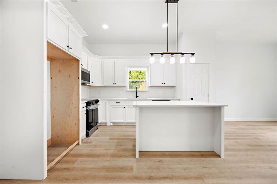 Kitchen with white cabinetry, a center island, light hardwood / wood-style floors, appliances with stainless steel finishes, and decorative light fixtures