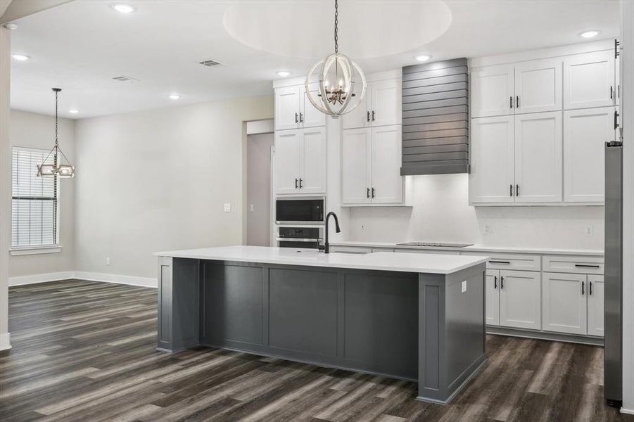 Kitchen with hanging light fixtures, dark hardwood / wood-style floors, white cabinetry, and a center island with sink