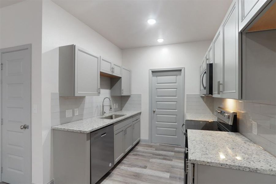 Kitchen with stainless steel appliances, tasteful backsplash, light stone countertops, light wood-type flooring, and sink