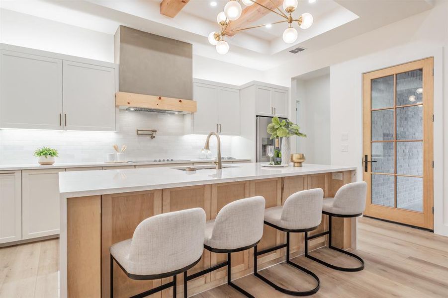 Kitchen with a center island with sink, a tray ceiling, blonde plank, wood-like luxury vinyl floors and backsplash