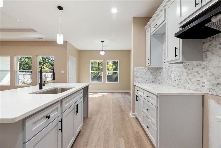 Kitchen with tasteful backsplash, white cabinetry, decorative light fixtures, sink, and light hardwood / wood-style floors