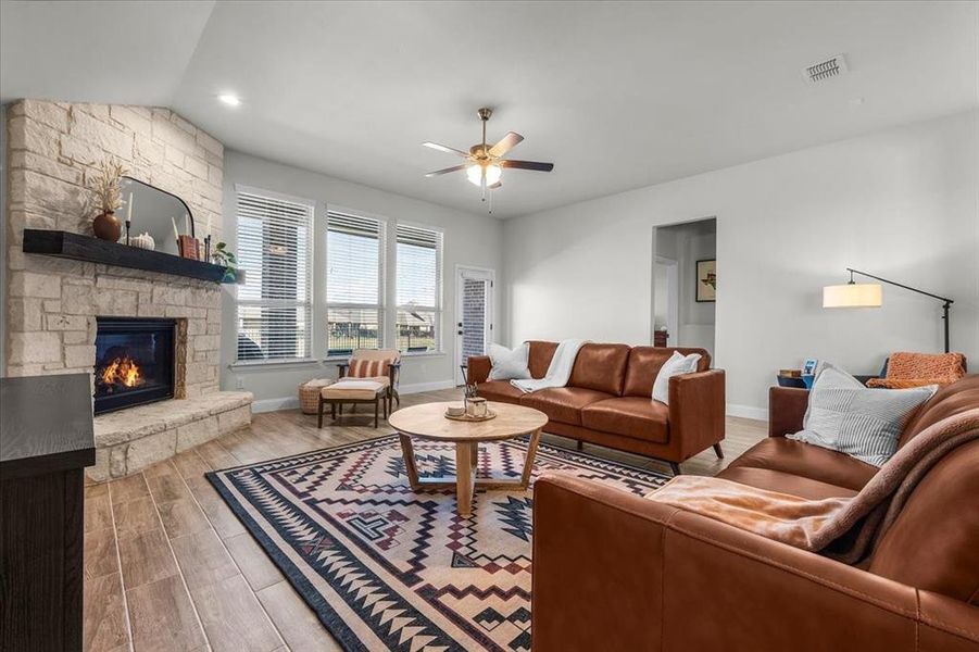 Living room featuring ceiling fan, light hardwood / wood-style floors, a stone fireplace, and lofted ceiling