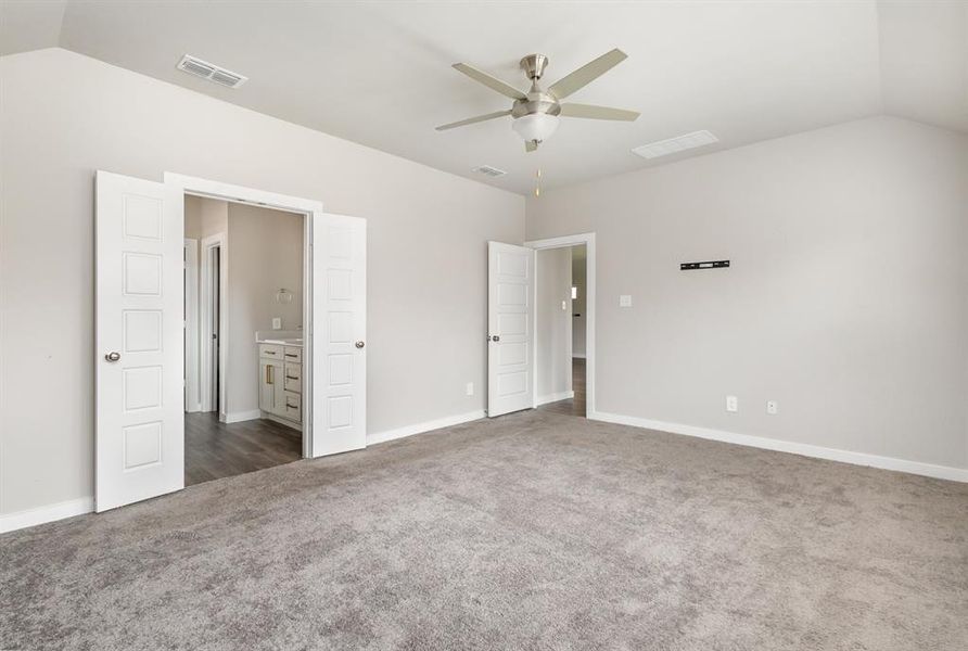 Unfurnished bedroom with dark colored carpet, ceiling fan, connected bathroom, and vaulted ceiling