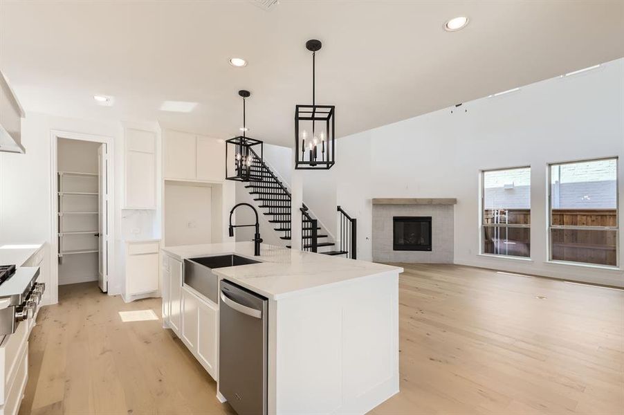 Kitchen with a kitchen island with sink, stainless steel appliances, decorative light fixtures, light wood-type flooring, and white cabinetry