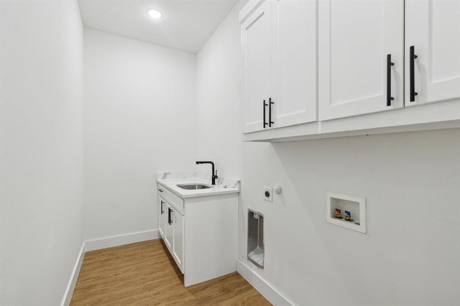 Washroom with light hardwood / wood-style floors, cabinets, hookup for a washing machine, electric dryer hookup, and sink