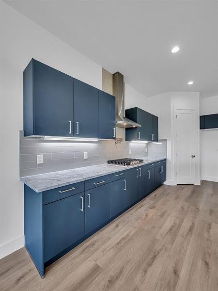 Kitchen featuring blue cabinetry, light hardwood / wood-style flooring, wall chimney range hood, and tasteful backsplash