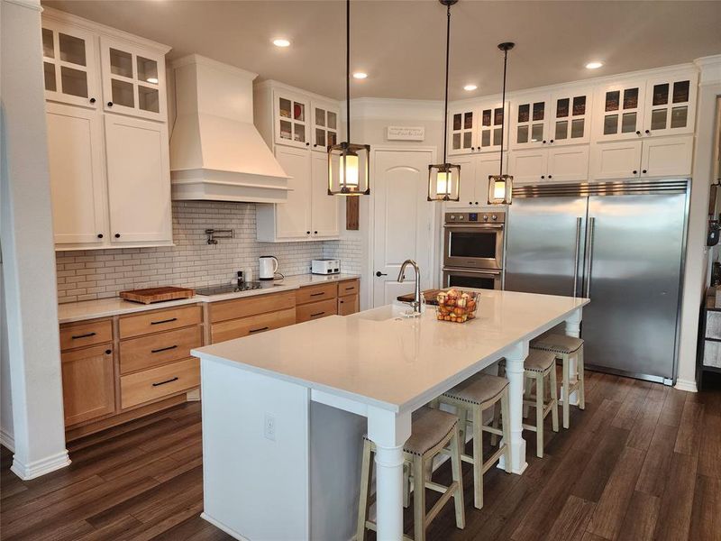 Kitchen with premium range hood, a kitchen island with sink, stainless steel appliances, and white cabinets