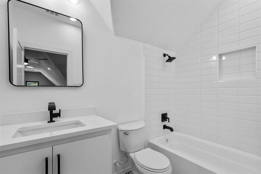 Full bathroom featuring vanity, tiled shower / bath combo, toilet, and vaulted ceiling