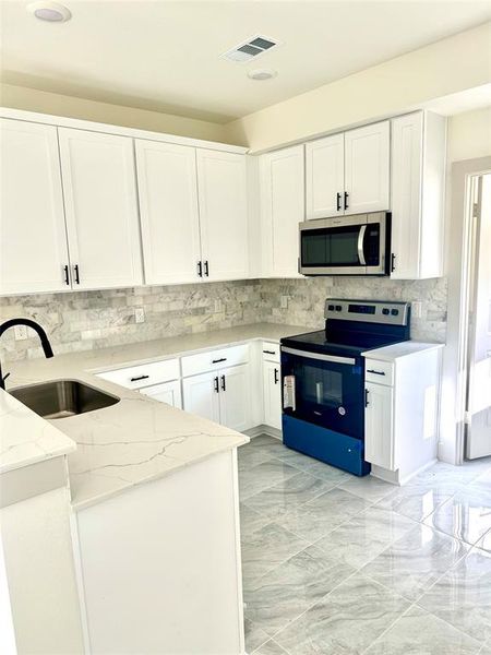 Kitchen with appliances with stainless steel finishes, white cabinets, light stone countertops, and sink