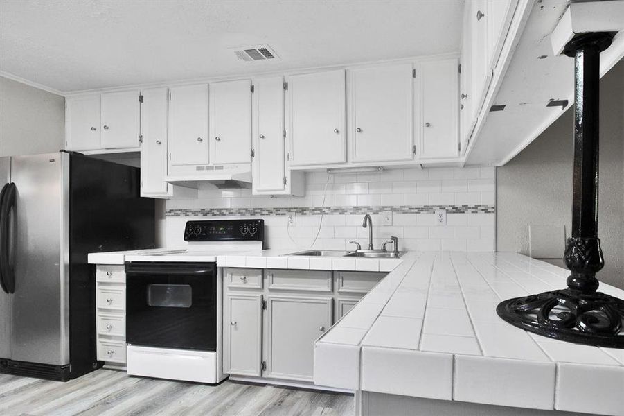 Kitchen featuring premium range hood, tile countertops, white cabinets, light hardwood / wood-style flooring, and white electric range oven