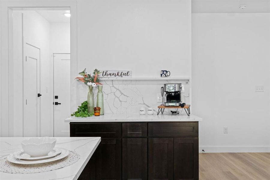 Bar featuring dark brown cabinetry, tasteful backsplash, light stone countertops, and light hardwood / wood-style flooring