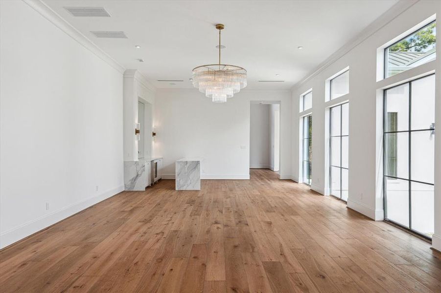 This expansive great room unites a sleek luxury bar, inviting living room, and elegant formal dining area for seamless entertaining. Durango Doors lead to a spacious covered patio, creating a perfect indoor-outdoor flow. White oak flooring and exquisite designer lighting enhance the room's sophisticated ambiance.