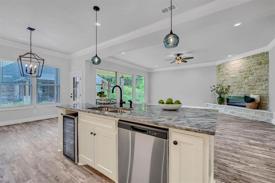 Kitchen with white cabinets, a stone fireplace, dishwasher, beverage cooler, and sink