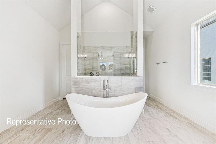 Bathroom with tile floors, a wealth of natural light, lofted ceiling, and a bath to relax in