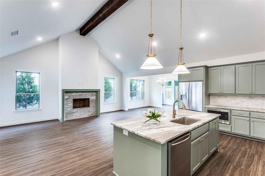 Kitchen with dark wood-type flooring, a center island with sink, appliances with stainless steel finishes, high vaulted ceiling, and sink