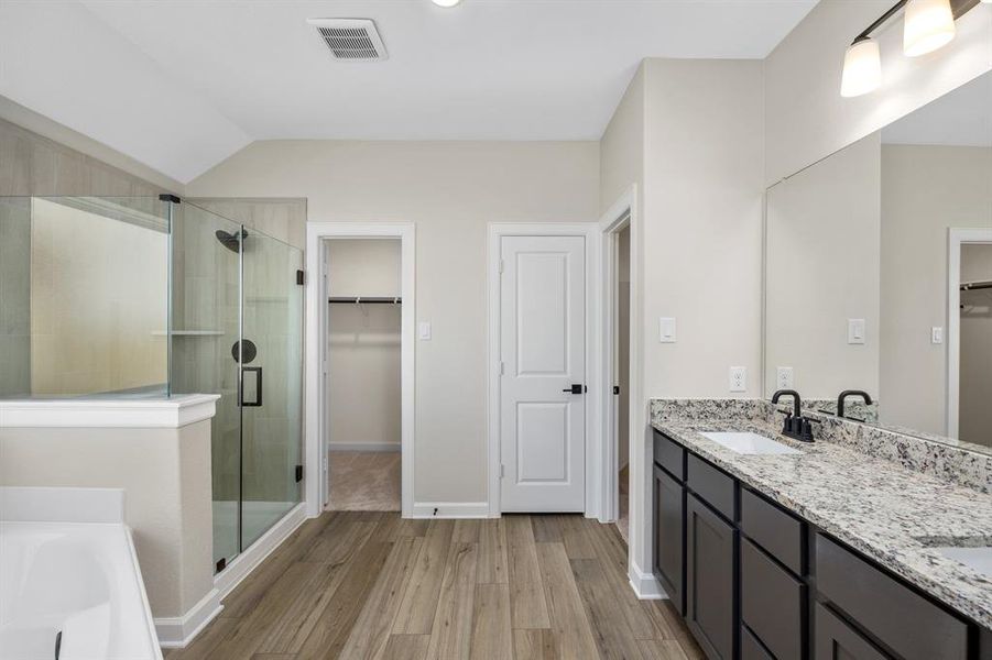 This luxurious bathroom features a sleek glass-enclosed tile walk-in shower, double granite vanity, and rich cabinetry. The wood-look flooring adds warmth, while the large walk-in closet and soaking tub make this space both practical and indulgent