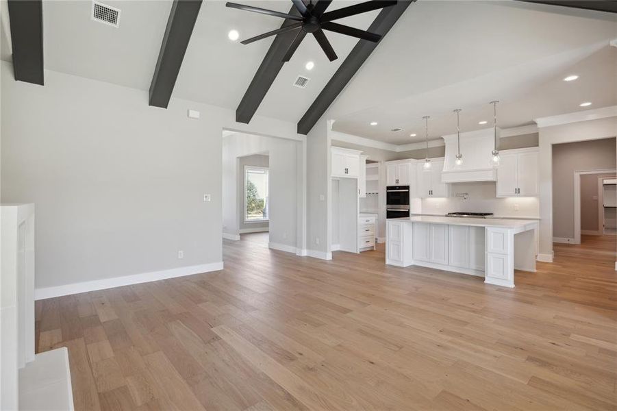 Unfurnished living room featuring light wood-type flooring, beamed ceiling, ceiling fan, and high vaulted ceiling