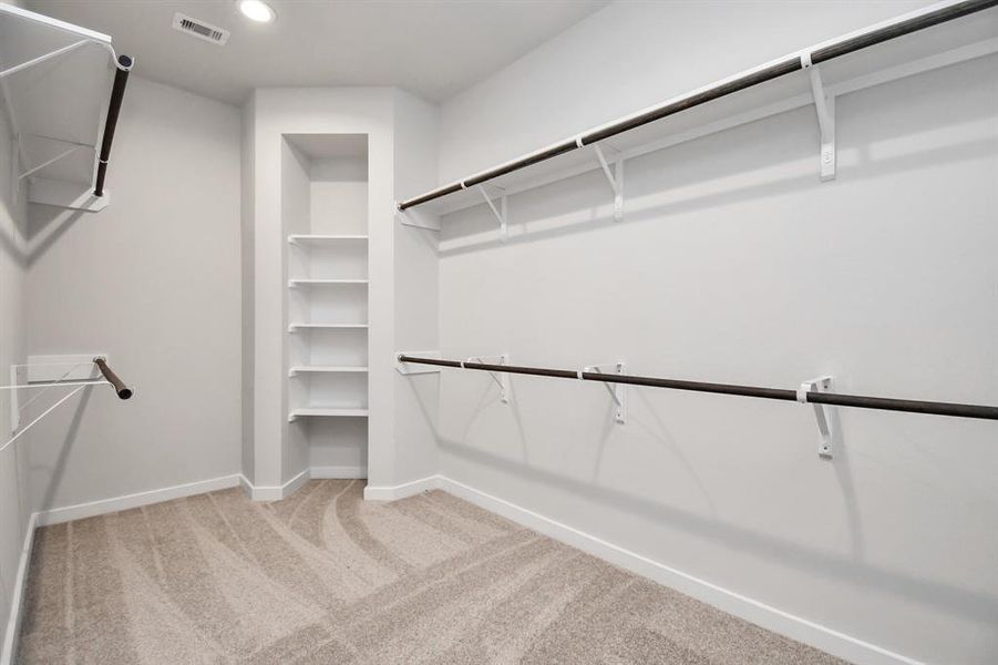 Roomy walk-in closet boasting high ceilings and plush carpeting. Let the inviting ambiance of warm paint tones surround you, make use of the practicality of built-in shelving, and revel in the contemporary and functional escape enriched by dark finishes. Sample photo of completed home with similar floor plan. Actual colors and selections may vary.