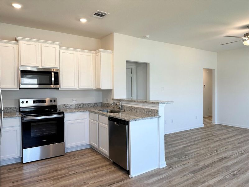 Kitchen includes granite countertops, luxury vinyl plank flooring, 36” upper cabinets with crown molding, a full suite of stainless-steel Whirlpool appliances – including refrigerator with ice maker, recessed lighting, and a large single basin sink.