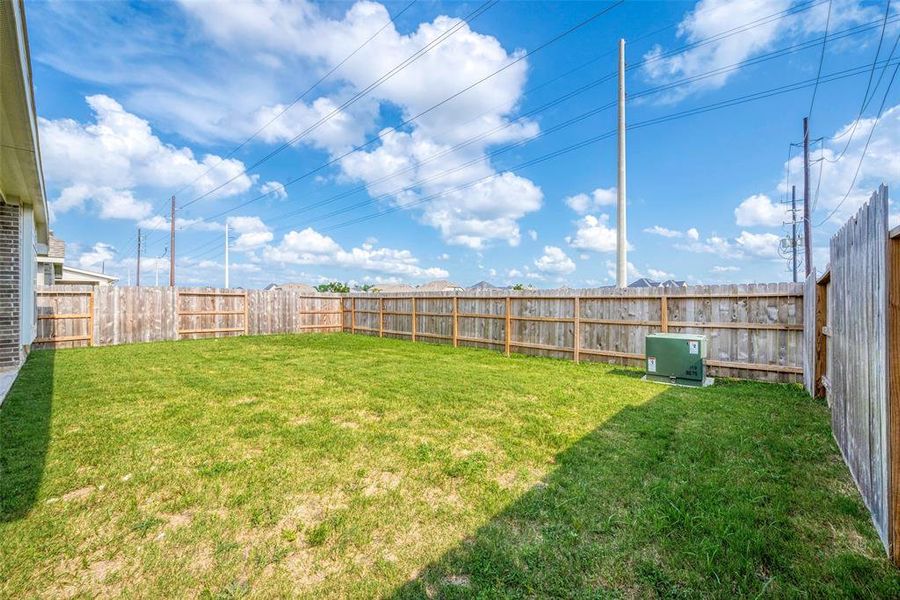 This expansive backyard with a sturdy fence provides ample space for outdoor activities, relaxation, and entertaining. The clear blue sky sets the scene for a perfect day enjoying the fresh air.