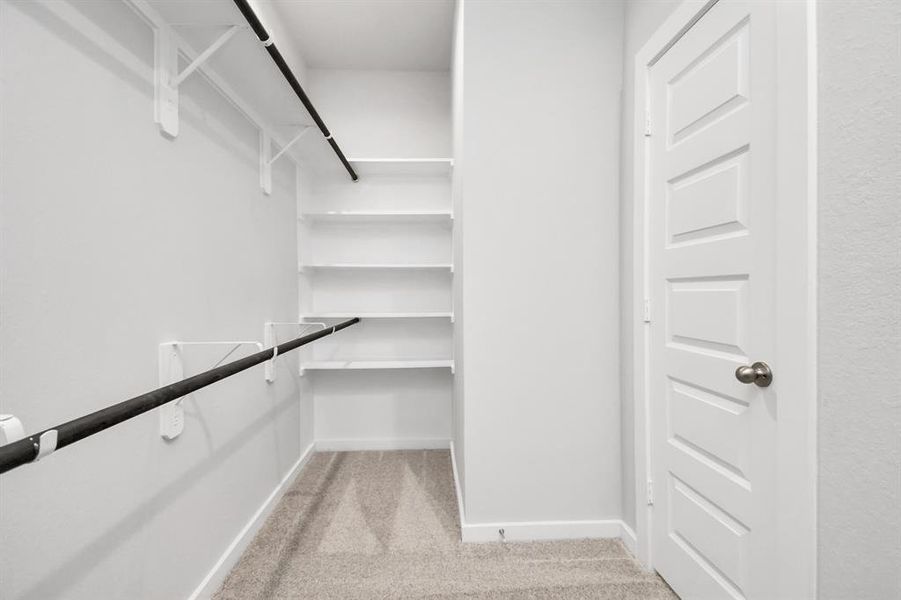 Step into a walk-in closet that defines luxury and functionality. This generously sized space boasts built-in shelving, providing ample room for organization. With high ceilings and recessed lighting, the ambiance is both bright and welcoming. Plush carpeting underfoot enhances the comfort, while warm paint tones add a touch of coziness. Sample photo of completed home with similar floor plan. As-built interior colors and selections may vary.