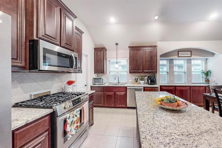 Kitchen featuring stainless steel appliances, a healthy amount of sunlight, tasteful backsplash, and vaulted ceiling