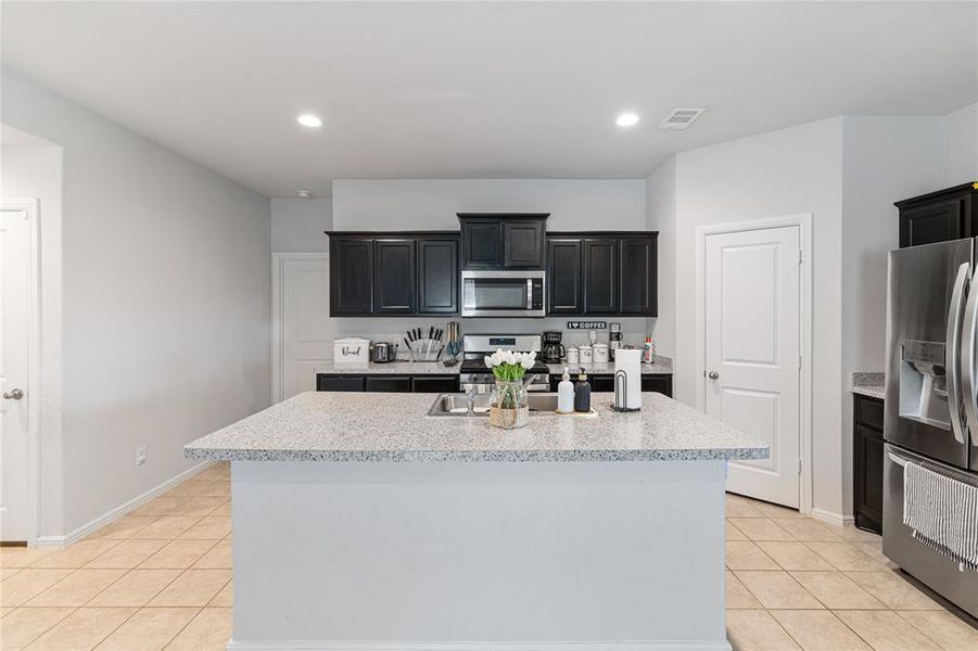 Kitchen with appliances with stainless steel finishes, light tile patterned flooring, a kitchen island with sink, and light stone counters