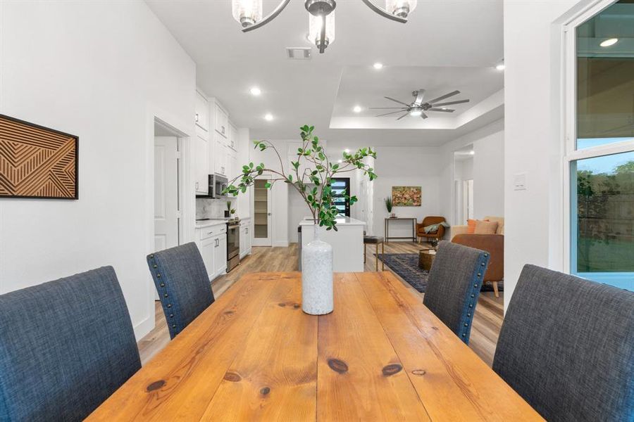 Dining room featuring ceiling fan with notable chandelier, light wood-type flooring, and a raised ceiling