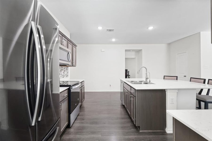 Kitchen with sink, dark wood-type flooring, a breakfast bar, a center island with sink, and appliances with stainless steel finishes