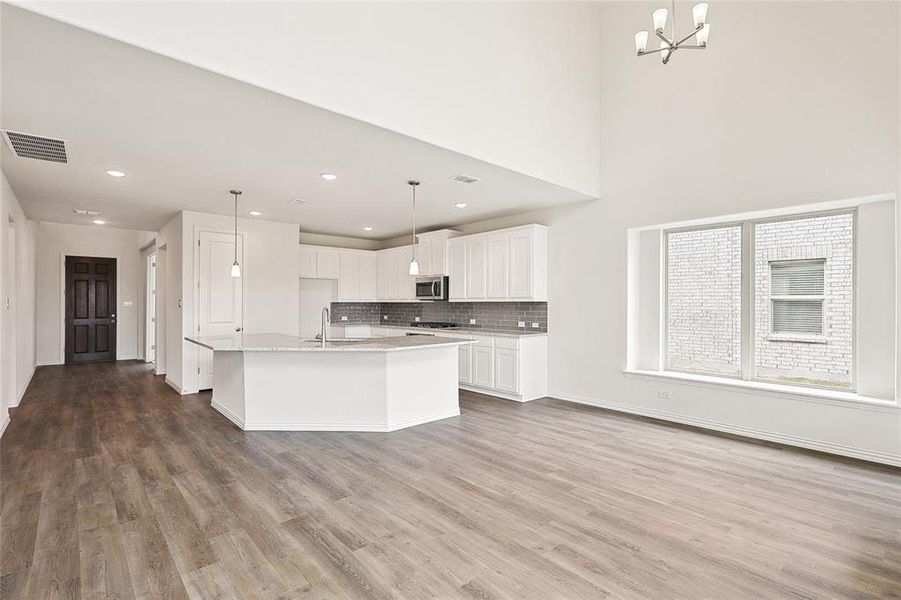 Kitchen with decorative light fixtures, a center island with sink, wood-type flooring, tasteful backsplash, and white cabinets