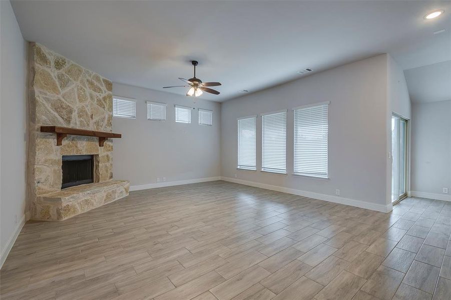 Unfurnished living room featuring a stone fireplace, light wood-type flooring, and ceiling fan