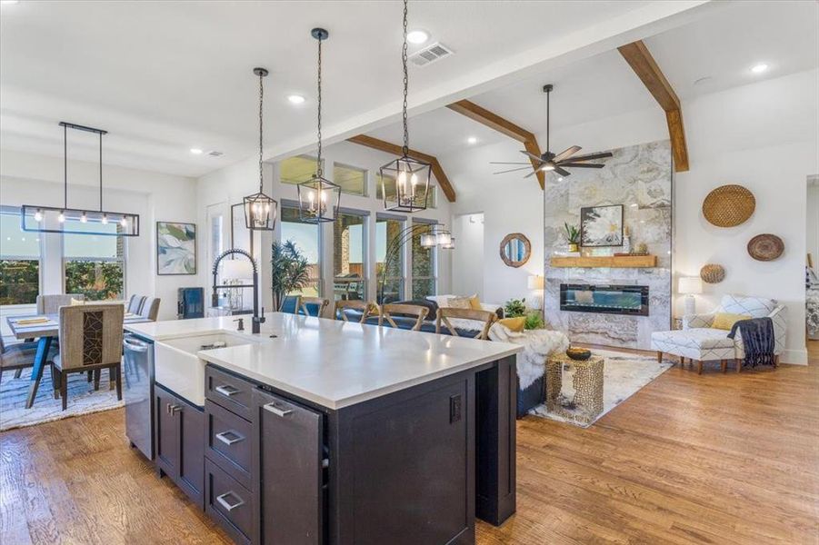 Kitchen with light hardwood / wood-style floors, a kitchen island with sink, sink, decorative light fixtures, and a stone fireplace