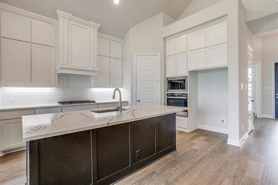 Kitchen featuring vaulted ceiling, black oven, built in microwave, a kitchen island with sink, and sink