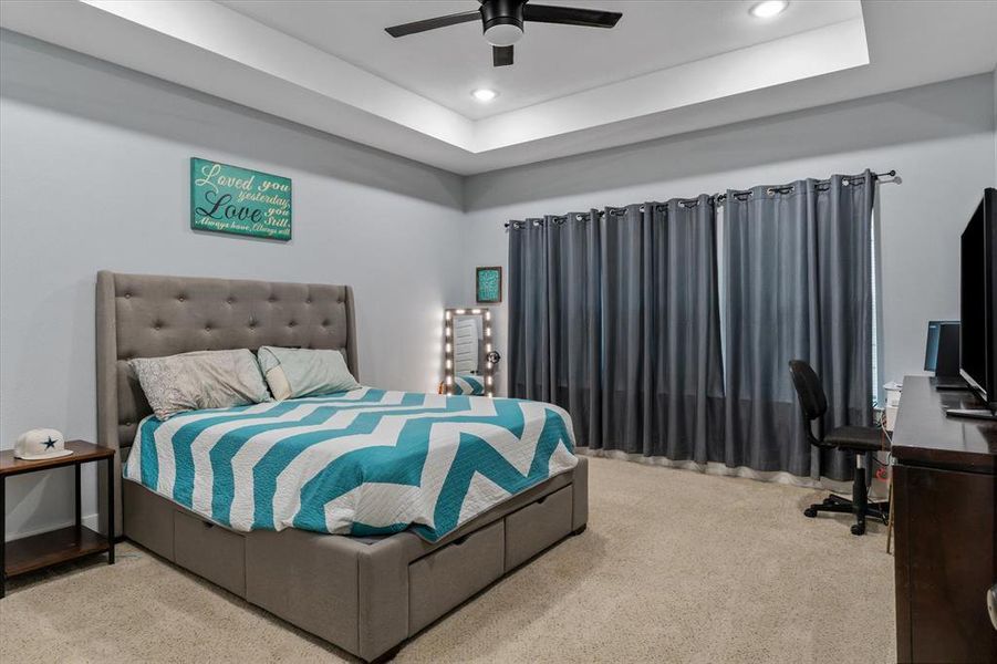 Bedroom with ceiling fan, a tray ceiling, and light carpet